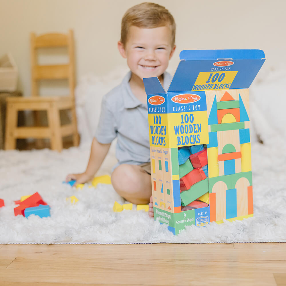 Boy sitting on run with a few blocks removed from the Melissa and Doug 100 Piece Wood Blocks Set box that is in front of him