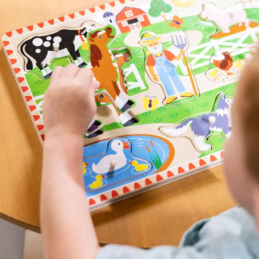 Child holding a wooden animal piece from Melissa & Doug Old MacDonald’s Farm sound puzzle, exploring texture and shape for early fine motor development and tactile learning experience.