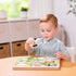 Child lifting a puzzle piece from the Melissa & Doug Old MacDonald’s Farm sound puzzle, a musical peg board that plays animal sounds when pieces are correctly placed, enhancing sensory learning.