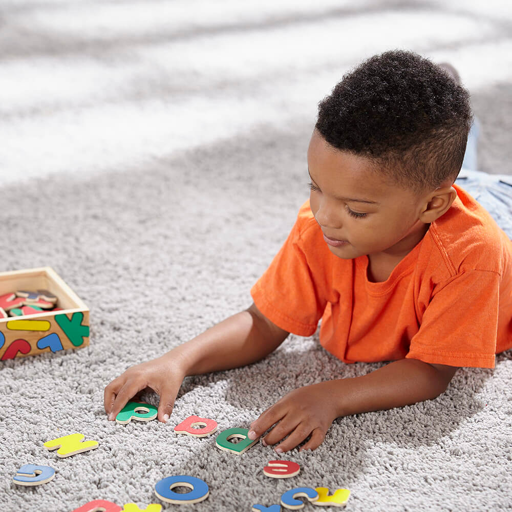 Boy playing with Melissa and Doug Wooden Letter Alphabet Magnets on the carpet