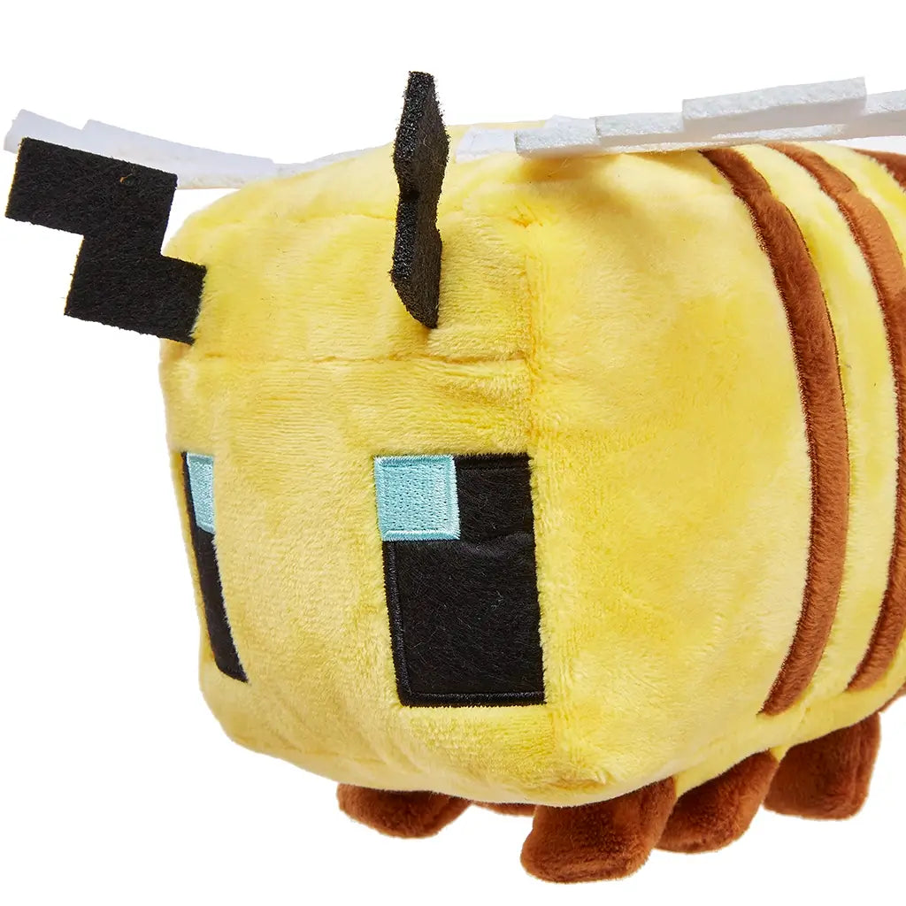 Minecraft bee plush close-up featuring yellow plush fabric, brown stripe detailing, square pixel-style eyes with blue accents, and felt antenna elements, emphasizing texture, stitching quality, and blocky game-inspired form against white.