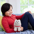 Child in red shirt smiles on couch while holding Minecraft Dennis plush wolf, highlighting soft beige fur, red collar, blocky cube-shaped design, and screen-accurate embroidered face.