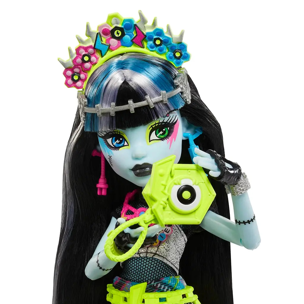 Close-up of Monster High Frankie Stein doll’s face with mismatched eye colors, bold makeup, silver crown, and neon flower headband for a striking festival look.