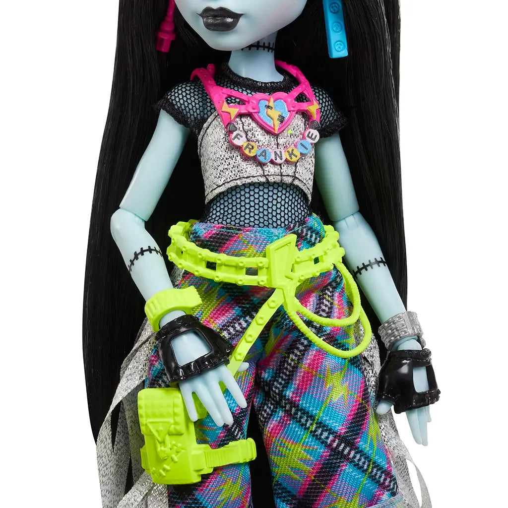Close-up of Frankie Stein doll’s outfit featuring mesh crop top, plaid multicolor pants, neon green belt with accessories, and detailed black and silver wristbands.