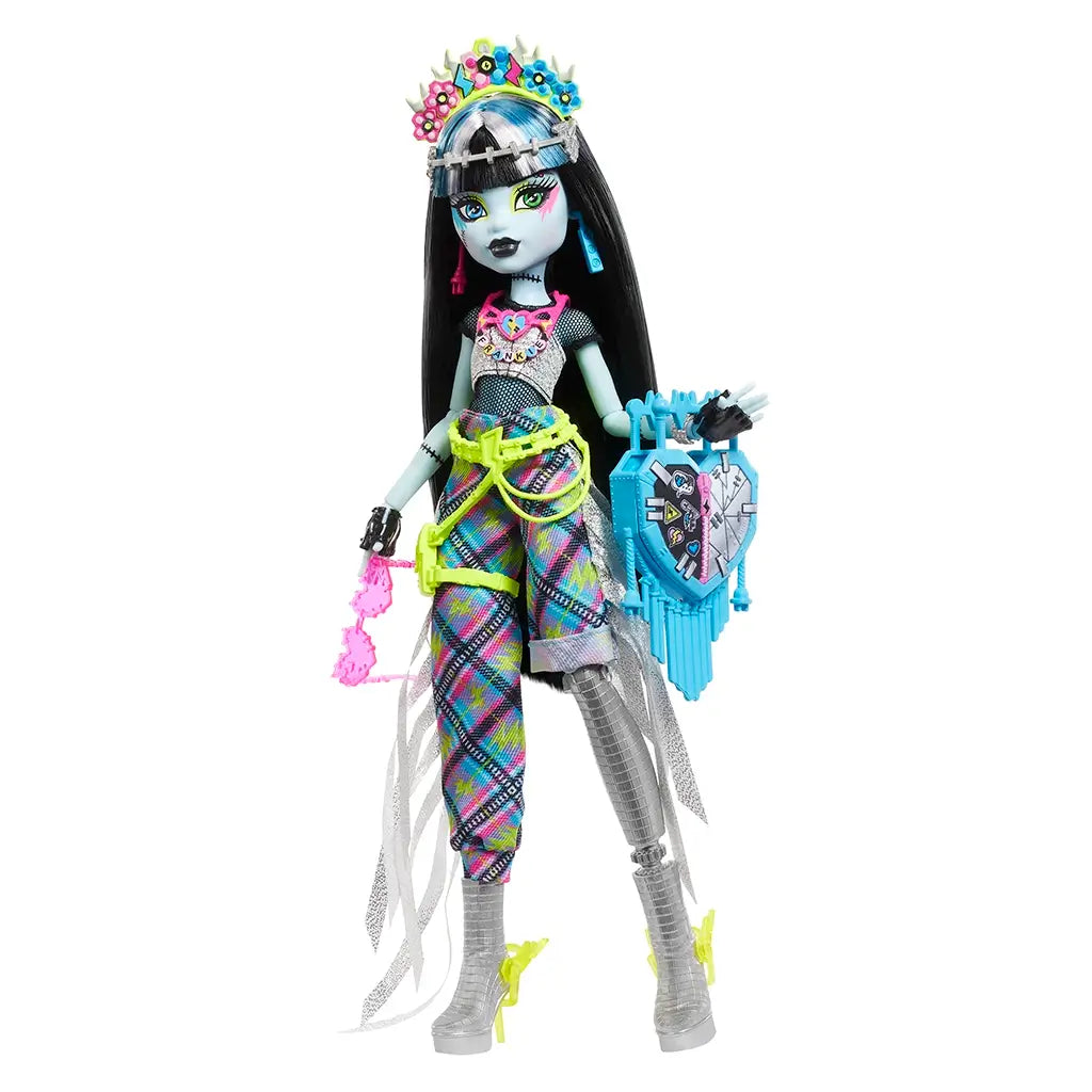 Monster High Frankie Stein doll wearing bright plaid pants, silver boots, and neon accessories, holding a blue heart-shaped bag with bold festival-themed details.