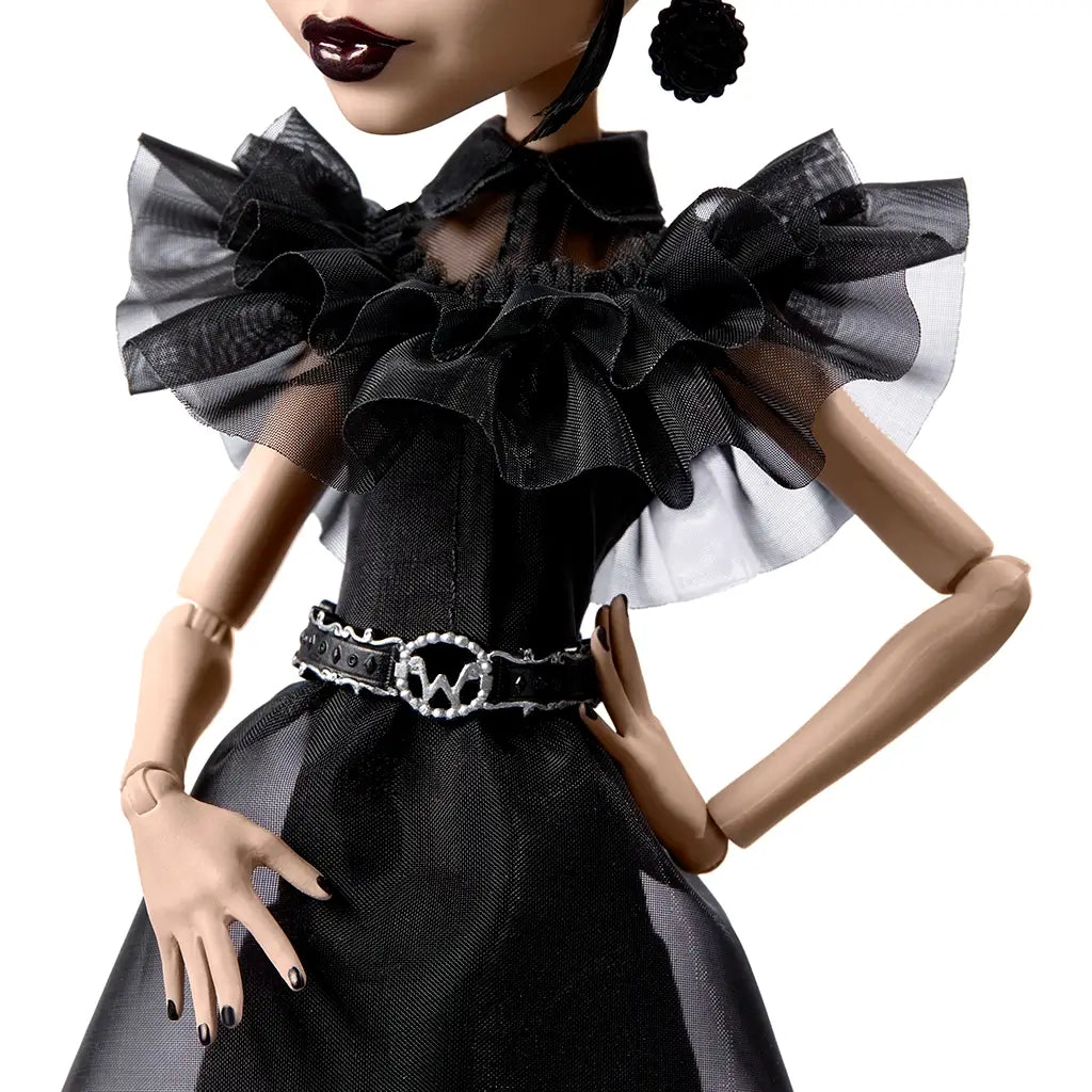 Close-up of Monster High Rave N’ Wednesday doll’s fitted black dress with layered sheer ruffles, high neckline, and silver skull belt detail, highlighting gothic-inspired fashion design.