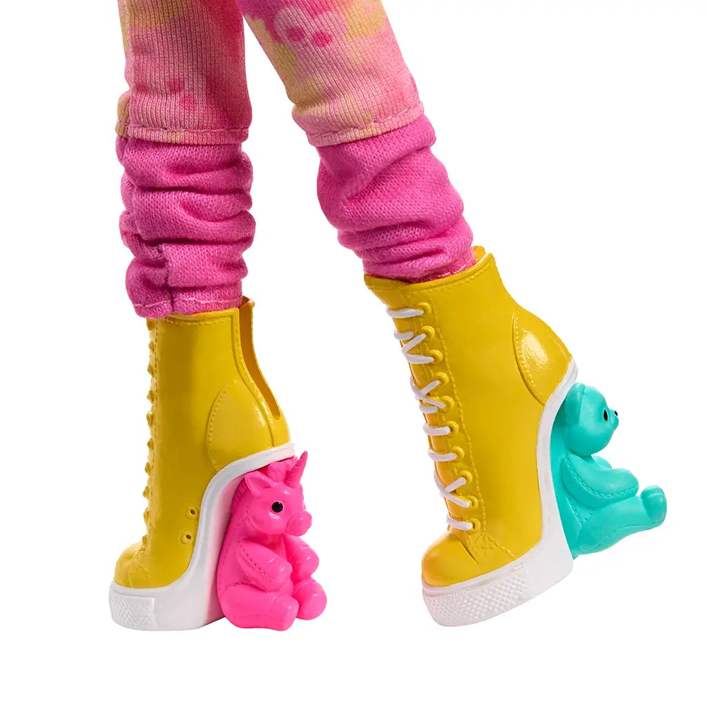 Close-up of Monster High Enid Sinclair doll’s yellow lace-up boots featuring sculpted pink unicorn and teal bear heels, paired with patterned pink leggings for a playful look.