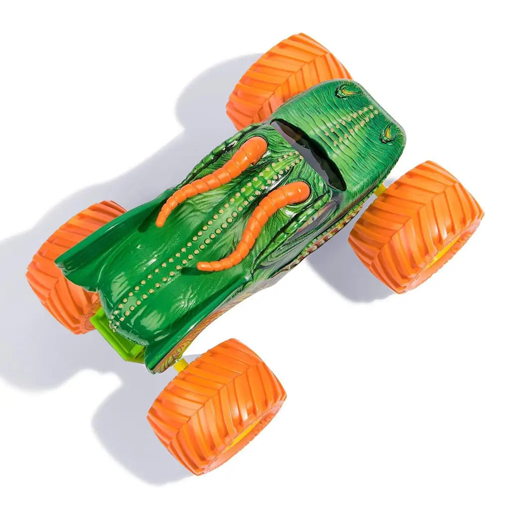 Top view of Monster Jam Dragon diecast truck shows sculpted green scaled body with raised fins, orange horns, dotted back detailing, and four large orange wheels positioned wide.