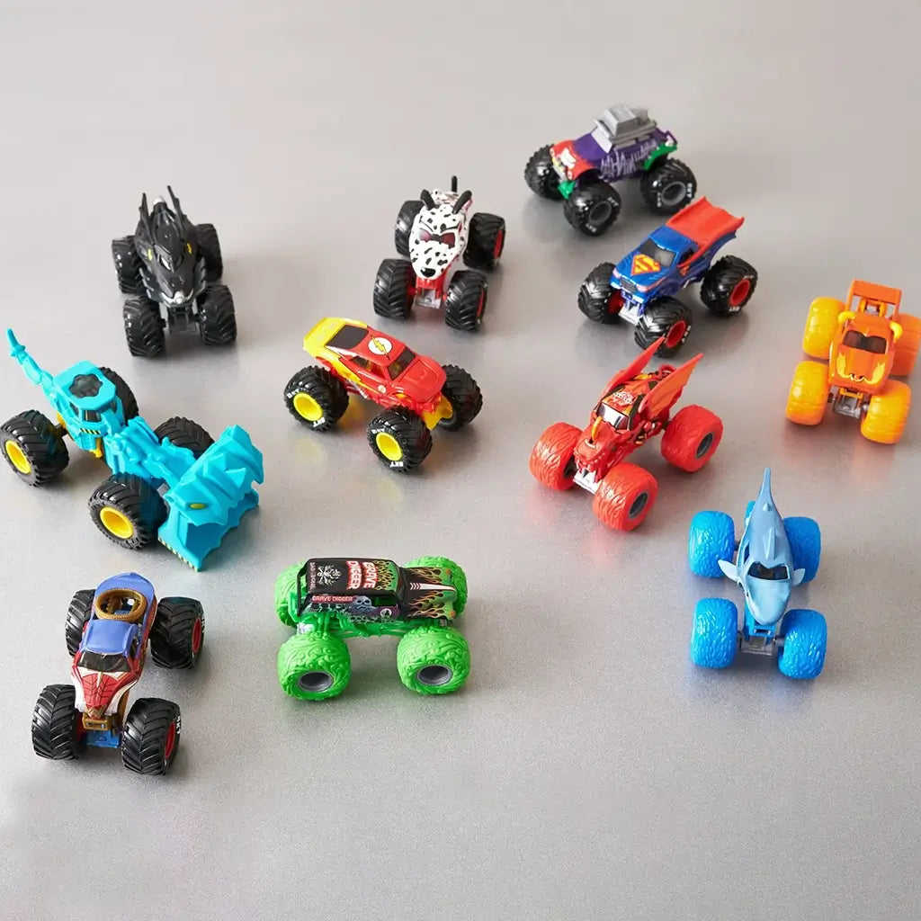 Monster Jam mini trucks collection in assorted bright plastic colors with varied character shapes and oversized wheels displayed in a scattered arrangement on a neutral tabletop.