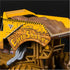Monster Jam Earth Shaker diecast truck closeup shows rugged yellow body with cracked rock graphics, raised dirt bed, and detailed suspension pipes against a dark background.