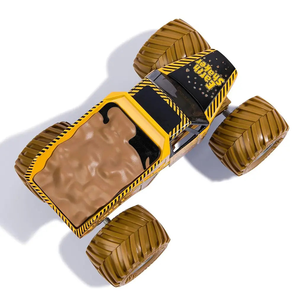 Top view of Monster Jam Earth Shaker diecast truck displays brown molded dirt load in the bed, yellow frame with caution stripes, and oversized wheels positioned at each corner.