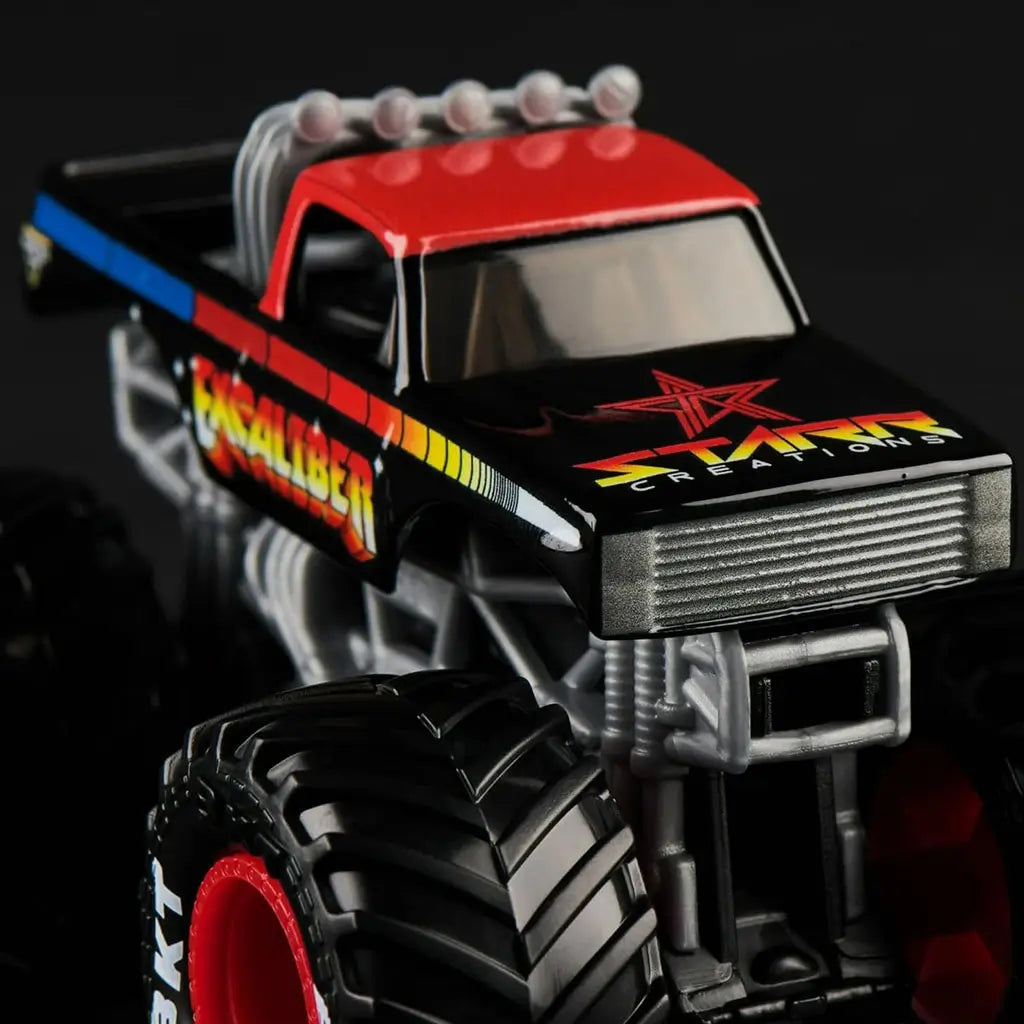 Close-up of Monster Jam Excaliber 1:64 diecast truck, featuring black body with rainbow gradient graphics, red roof, and oversized tread tires with red rims.