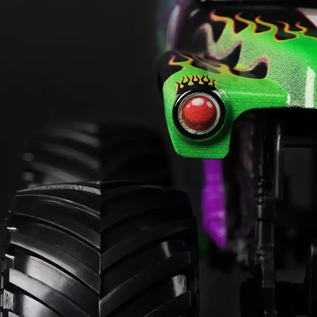 Closeup detail of Monster Jam Grave Digger diecast truck front corner, highlighting green flame paint, red circular headlight, and rugged black treaded tire.