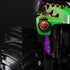 Closeup detail of Monster Jam Grave Digger diecast truck front corner, highlighting green flame paint, red circular headlight, and rugged black treaded tire.