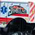 Monster Jam Jambulance Everyday Hero 1:64 scale toy truck close-up view highlighting side graphics with ambulance theme, red stripes, blue star emblem, and bold lettering.