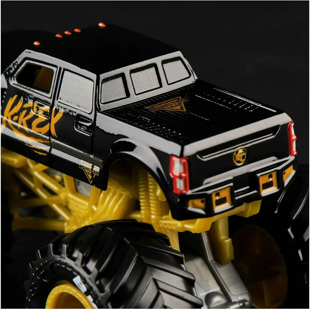 Closeup of Monster Jam Kane Brown K-Rex 1:64 scale diecast truck, featuring glossy black body with orange accents, gold chassis, and oversized rugged black tires.