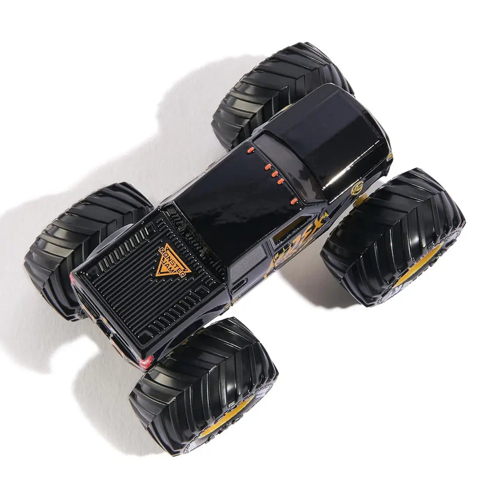 Top view of Monster Jam Kane Brown K-Rex diecast truck at 1:64 scale, showing glossy black roof, orange “K-Rex” graphics, gold chassis, and rugged black wheels.