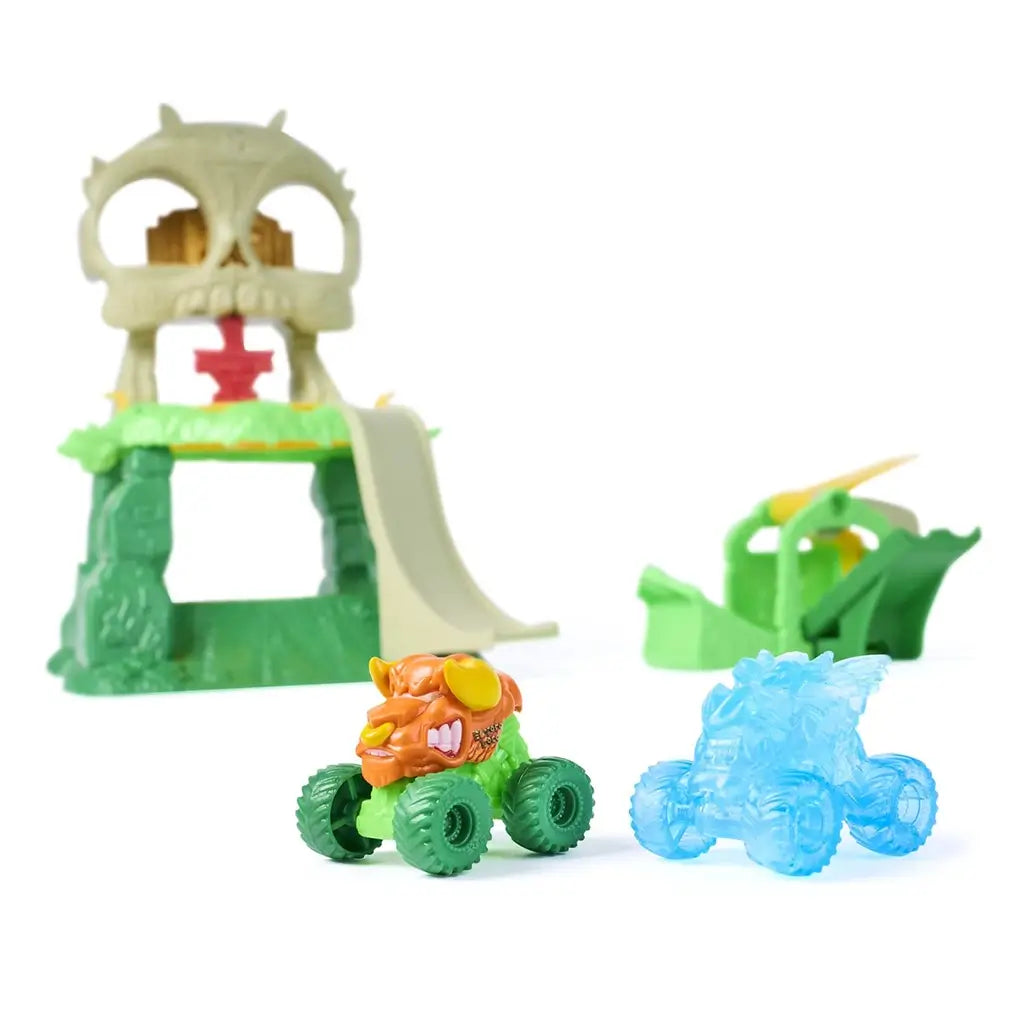 Monster Jam Mini Jams characters featuring El Toro Loco mini truck in green and orange plastic and translucent blue Dragon mini truck, shown in front of jungle skull playset pieces for imaginative monster truck play.