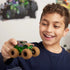 Monster Jam Mystery Mudders toy truck in green and brown plastic with muddy textured tires, oversized monster truck shape for play, held by a smiling child in an indoor playroom setting.