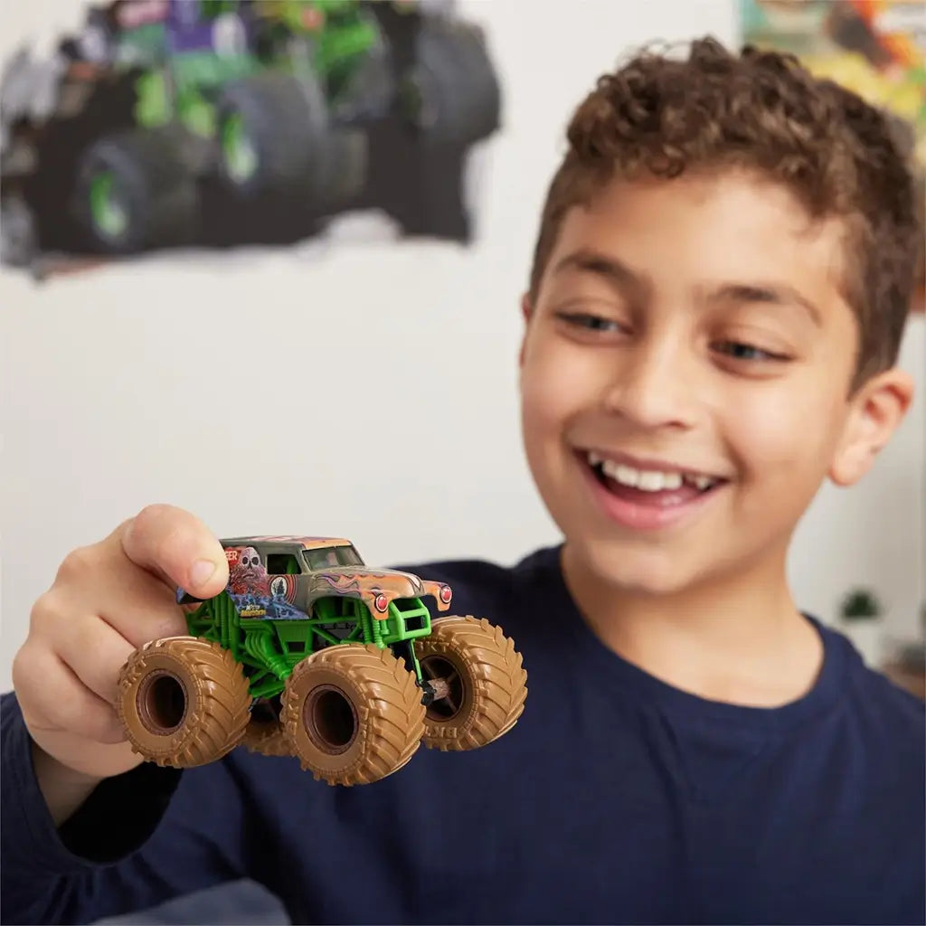 Monster Jam toy truck coated in brown mud with plastic body, chunky rubber tires, and compact form, held by a smiling child during play, demonstrating interactive use indoors with a softly blurred background.