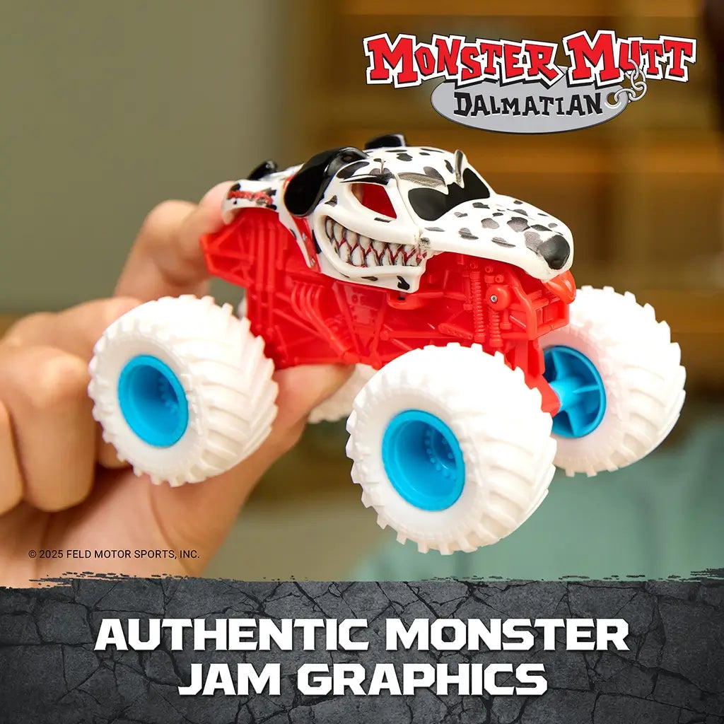 Monster Jam Monster Mutt Dalmatian toy truck red plastic frame with white and black spotted dog body and blue wheels held in hand, highlighting authentic graphics and detailed design in indoor setting
