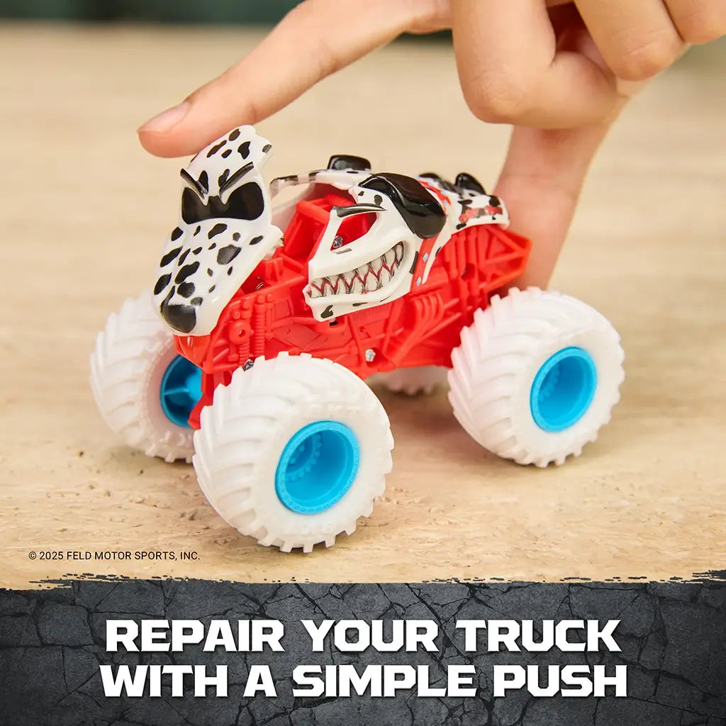Monster Jam Monster Mutt Dalmatian toy truck red plastic body with white and black spotted dog-themed shell and blue wheels, shown being pressed to repair after crash on a wooden tabletop background