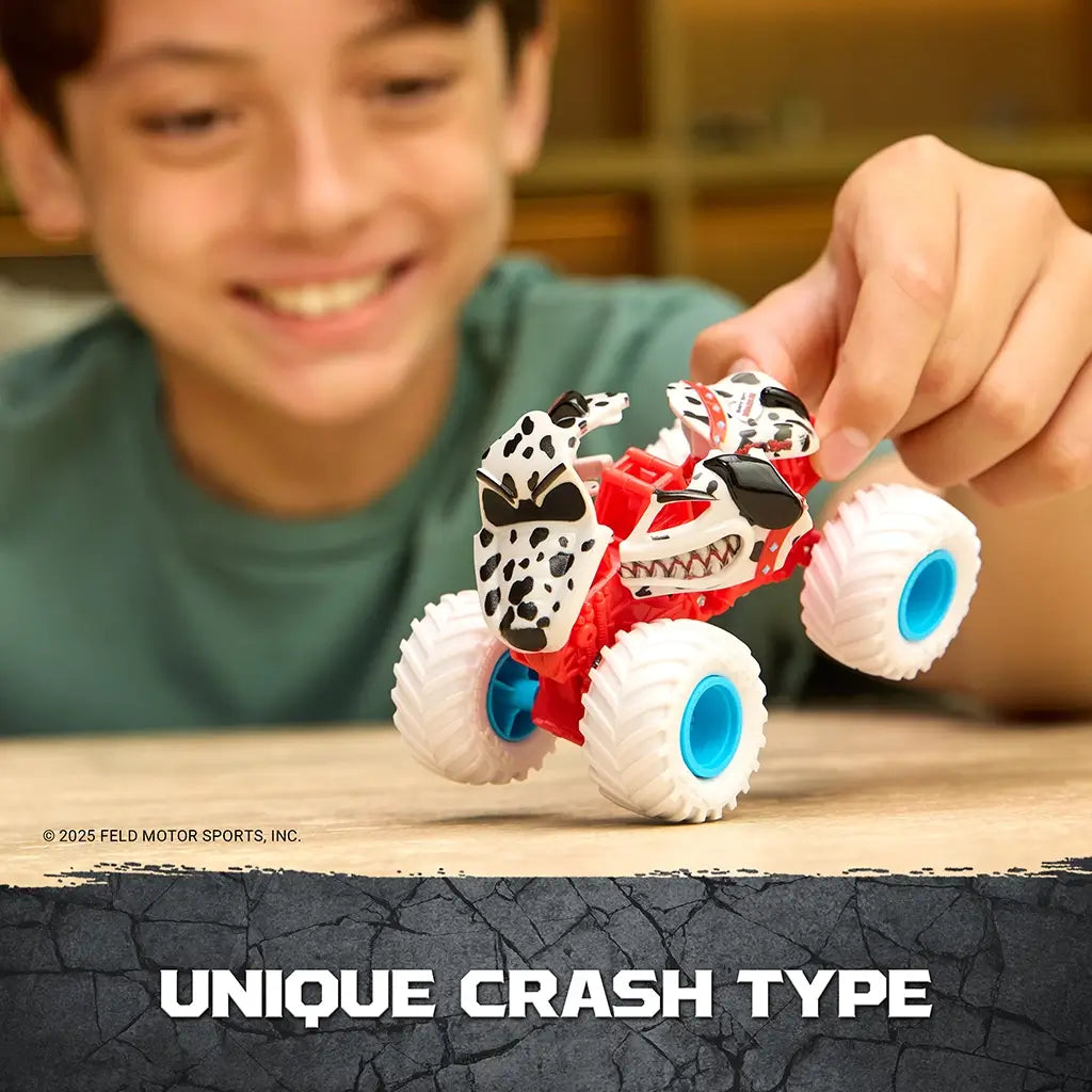 Monster Jam Monster Mutt Dalmatian toy truck red plastic frame with white spotted dog shell and blue wheels lifted by a child’s hand, demonstrating unique crash and reset play feature in indoor setting