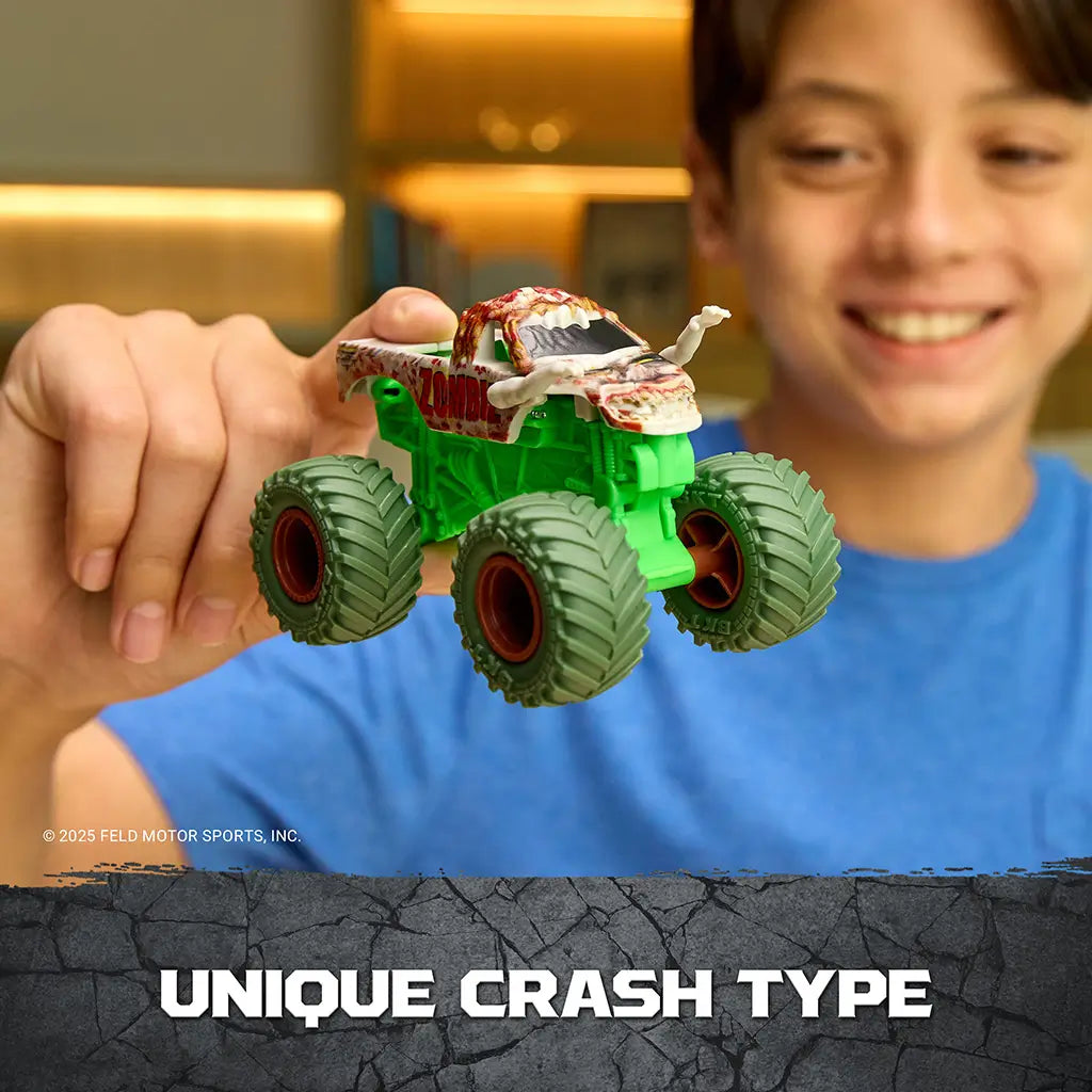 Monster Jam Zombie toy truck in green plastic with gray and red zombie details, flexible monster truck form with detachable crash parts, shown held by a child demonstrating unique crash feature indoors.