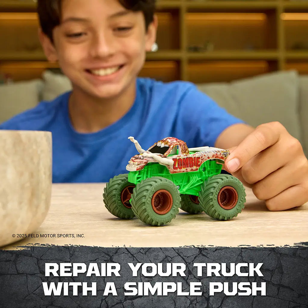 Monster Jam Zombie toy truck in green plastic with gray zombie details and red accents, oversized monster truck shape, shown being pressed to repair parts on a tabletop indoor play setting.