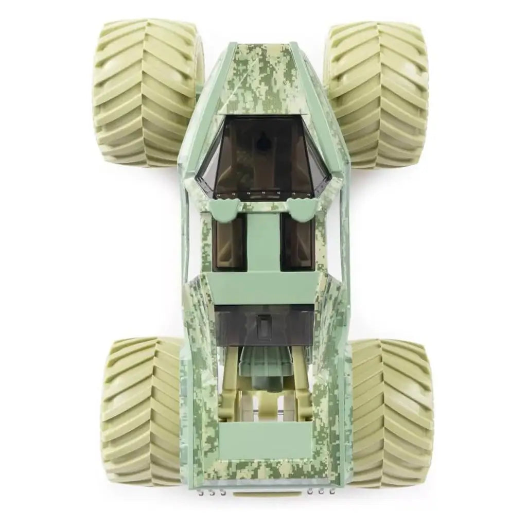Top view of Monster Jam Soldier Fortune diecast truck shows desert camouflage pattern, tinted cab windows, and oversized beige wheels arranged in wide stance around rugged frame.