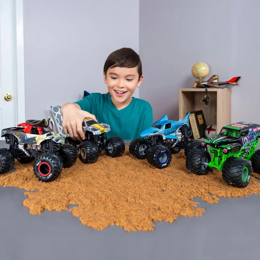 A smiling child plays with the Monster Jam Son-Uva Digger diecast truck on textured brown terrain, showcasing large BKT tires, blue chassis, and bold graphic bodywork in a cozy indoor playroom.