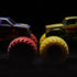 Monster Jam Marvel trucks in yellow and purple die-cast metal with oversized rubber tires, Wolverine and Sentinels designs facing each other, dramatic lighting on a dark studio background.