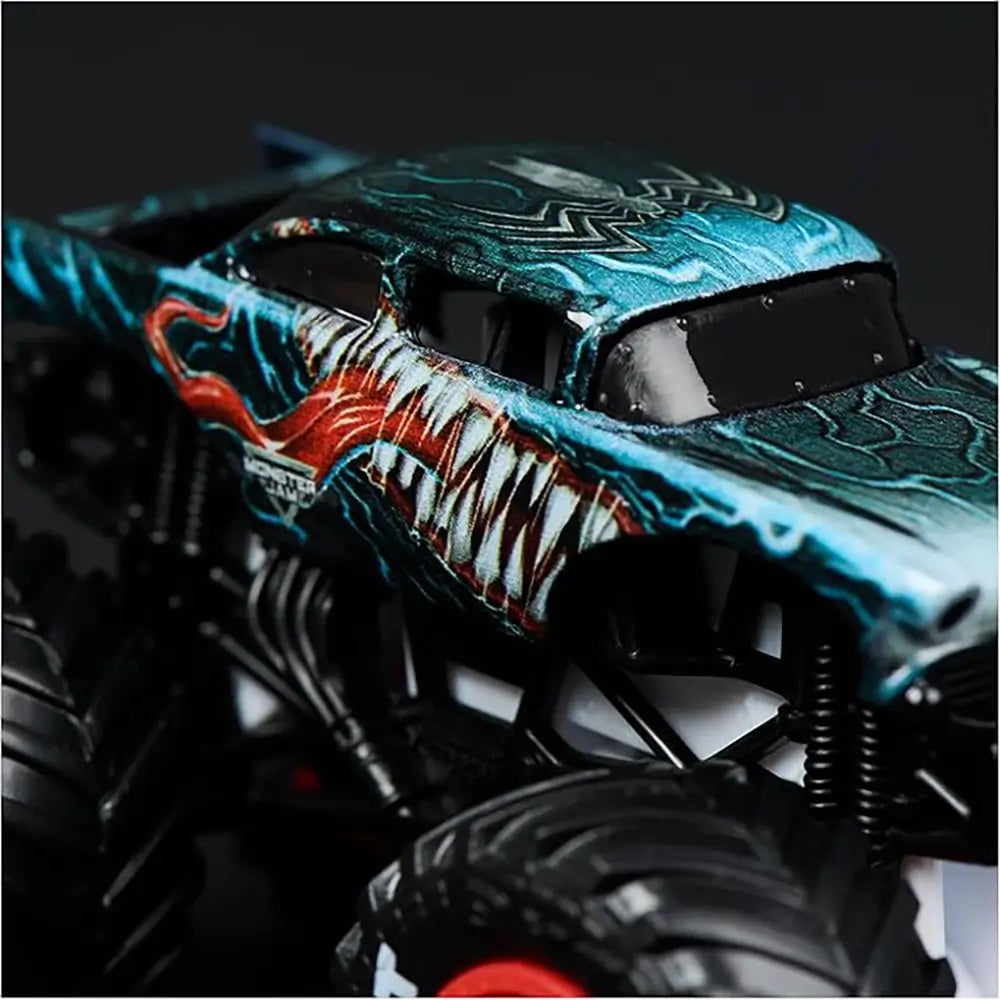 Monster Jam Venom truck close-up showing black and teal glossy metal body with sharp teeth graphics, detailed texture, oversized rubber tires, and suspension parts on a dark background.