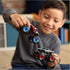 Monster Jam toy truck play scene with a young boy holding red and black die-cast trucks with large rubber tires, Spider-Man and Venom themes, indoors against a softly blurred home background.