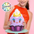 Close-up of a scented Disney Munchlings Ursula plush cupcake from The Little Mermaid, showing a purple base, white whipped top, yellow crown, and embroidered smiling face held by a person in red top.