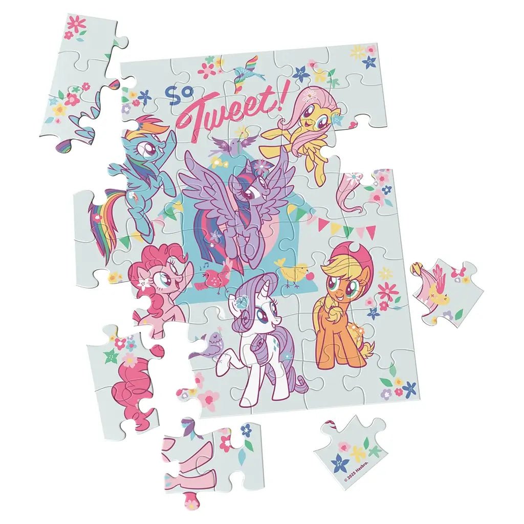 My Little Pony jigsaw puzzle featuring pastel multicolor cardboard pieces in interlocking shapes, showing cartoon ponies and flowers on a light blue background, partially assembled on a flat surface.