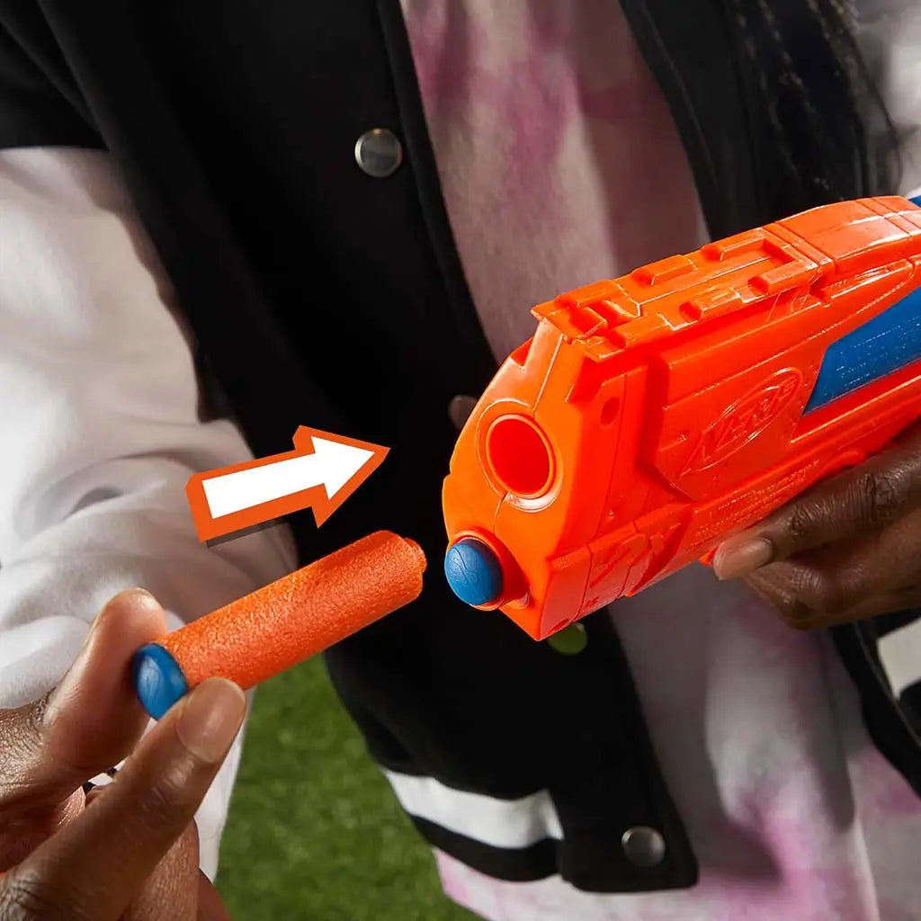 NERF blaster close-up shows orange textured plastic muzzle and round blue-tipped foam dart being loaded, with arrow graphic indicating insertion while player holds the compact toy in natural lighting. Described in clear detail for accessibility and user understanding.