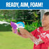 Smiling boy in red shirt spraying foam with a Nerf Super Soaker Foam Fury blaster outdoors, surrounded by green grass and trees, with “Ready, Aim, Foam!” slogan above.