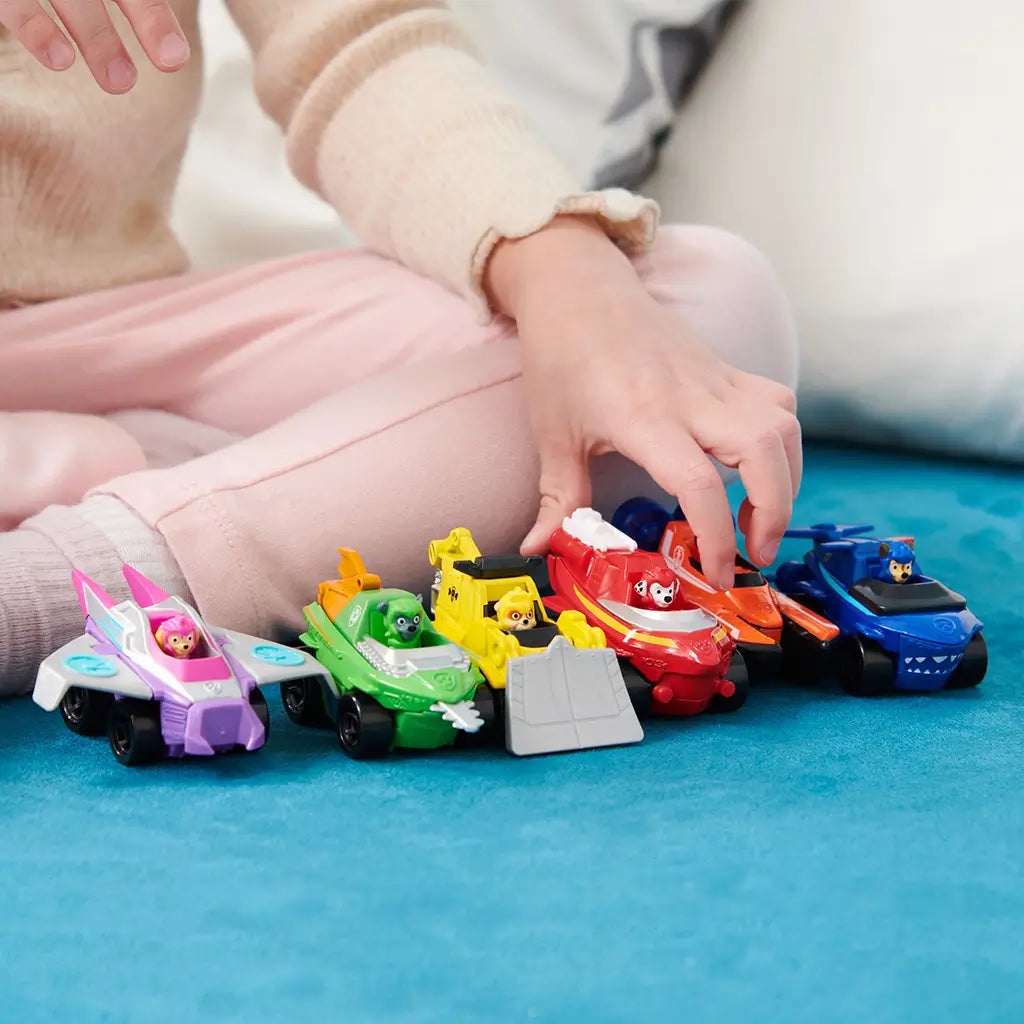 PAW Patrol toy vehicles in bright multicolor plastic and metal finishes, small rounded car and boat shapes for imaginative rescue play, child’s hands arranging figures on a soft teal play mat in a cozy indoor setting