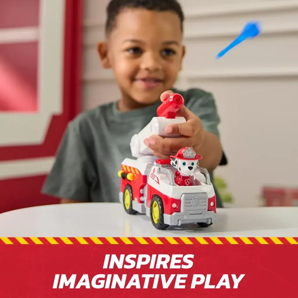 PAW Patrol Marshall fire truck toy in glossy red and white plastic with mounted launcher, operated by a smiling child at a table, demonstrating projectile action for creative rescue storytelling.