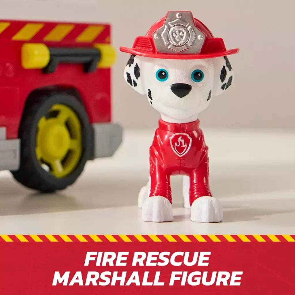 PAW Patrol Marshall fire rescue figure in bright red plastic uniform with silver badge helmet and white Dalmatian spots, standing upright beside a red fire truck on a neutral tabletop background.
