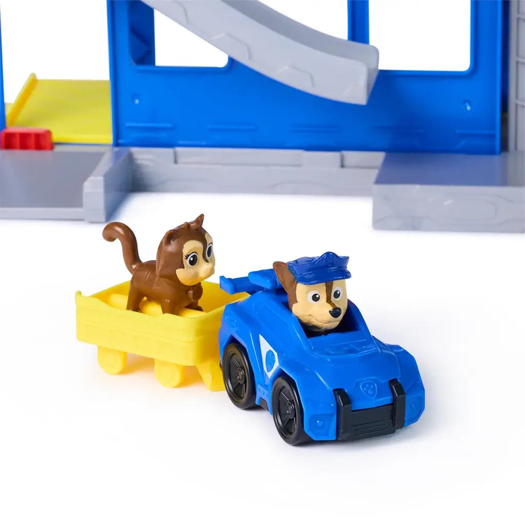 PAW Patrol Pup Squad police car toy in blue plastic with black wheels and yellow trailer, small animal figure riding inside, rescue vehicle accessory set displayed on a clean white background.