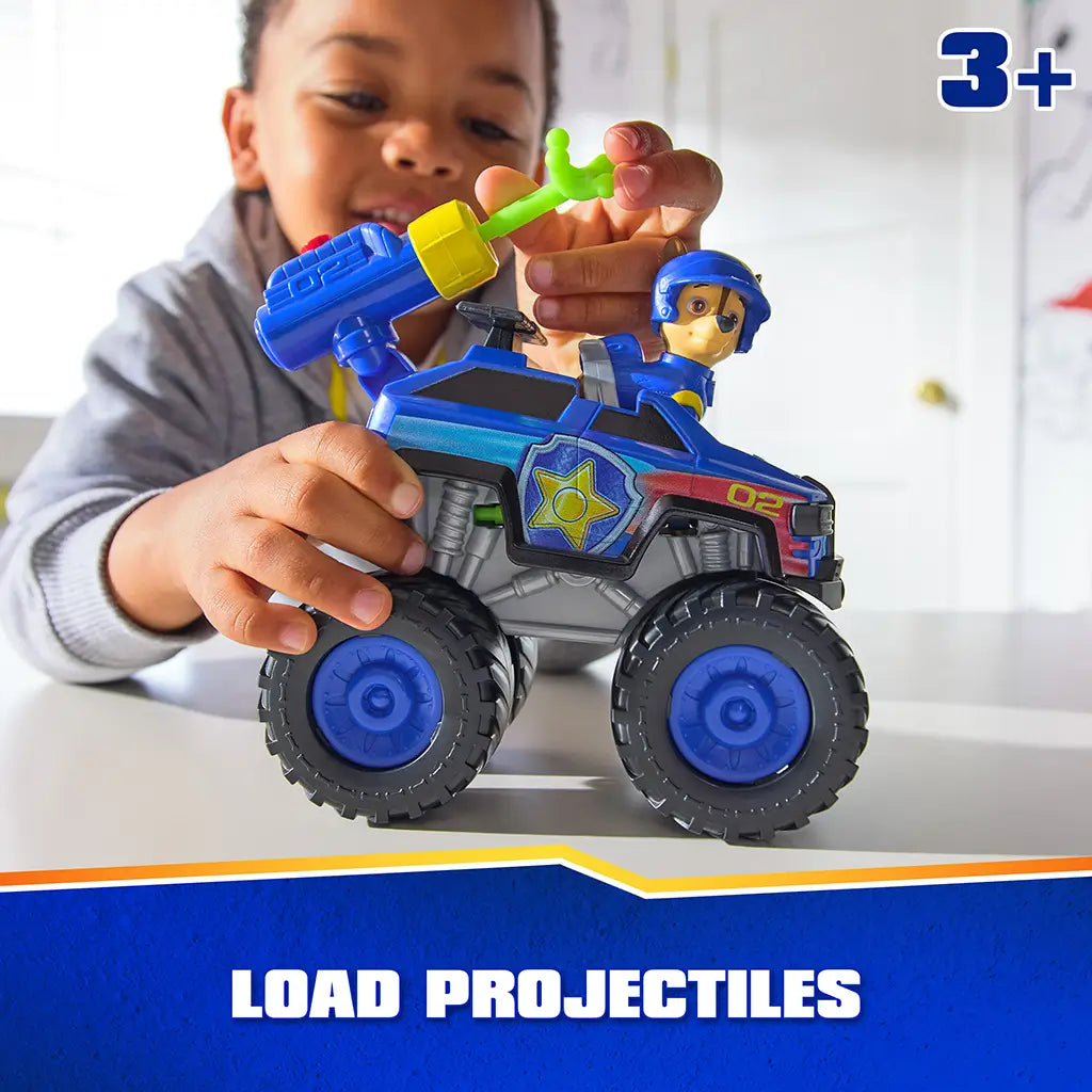 PAW Patrol toy truck blue plastic rescue vehicle with yellow launcher and green projectiles, Chase figure seated inside, child loading projectile on top in well lit indoor play setting.