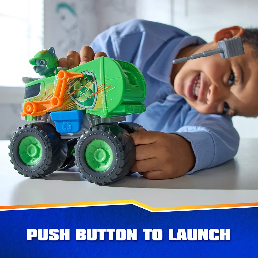 PAW Patrol Rocky recycle truck toy displays bright green plastic body with smooth finish, oversized wheels, and push-button launcher feature, demonstrated by a child during interactive tabletop play activity.