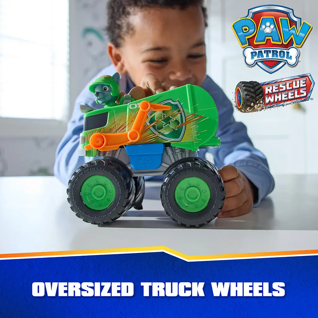 PAW Patrol Rocky recycle truck toy shows bright green plastic body with smooth finish, large oversized truck wheels, and recycling graphics, held by a child to highlight rugged design in indoor setting.