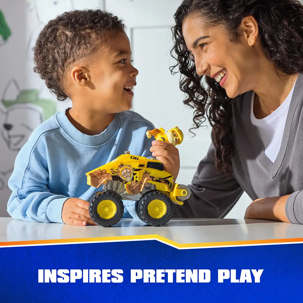 PAW Patrol Rubble bulldozer toy shows bright yellow plastic vehicle with textured details and oversized wheels, used by a child and parent together, highlighting interactive pretend play in a home setting.