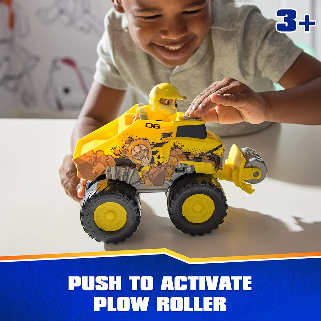 PAW Patrol Rubble bulldozer toy features bright yellow plastic body with rugged textures, large wheels, and front plow roller, activated by pressing top button during play on a tabletop surface.