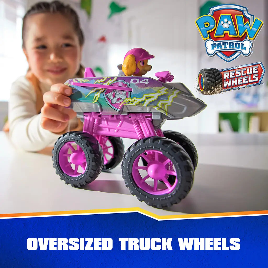 PAW Patrol Skye truck jet toy shows pink and gray plastic body with lightning graphics, chunky oversized wheels, and aircraft styling, held by a child during tabletop play in a bright indoor setting.