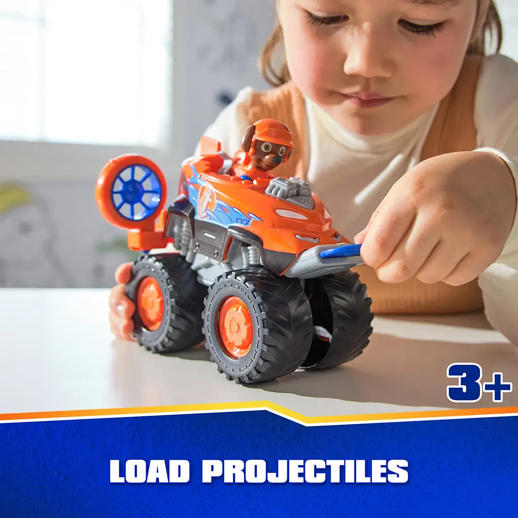 PAW Patrol Zuma hovercraft toy features bright orange plastic body with smooth and textured surfaces, oversized wheels, and projectile launcher discs, shown in child’s hands during tabletop play scene.