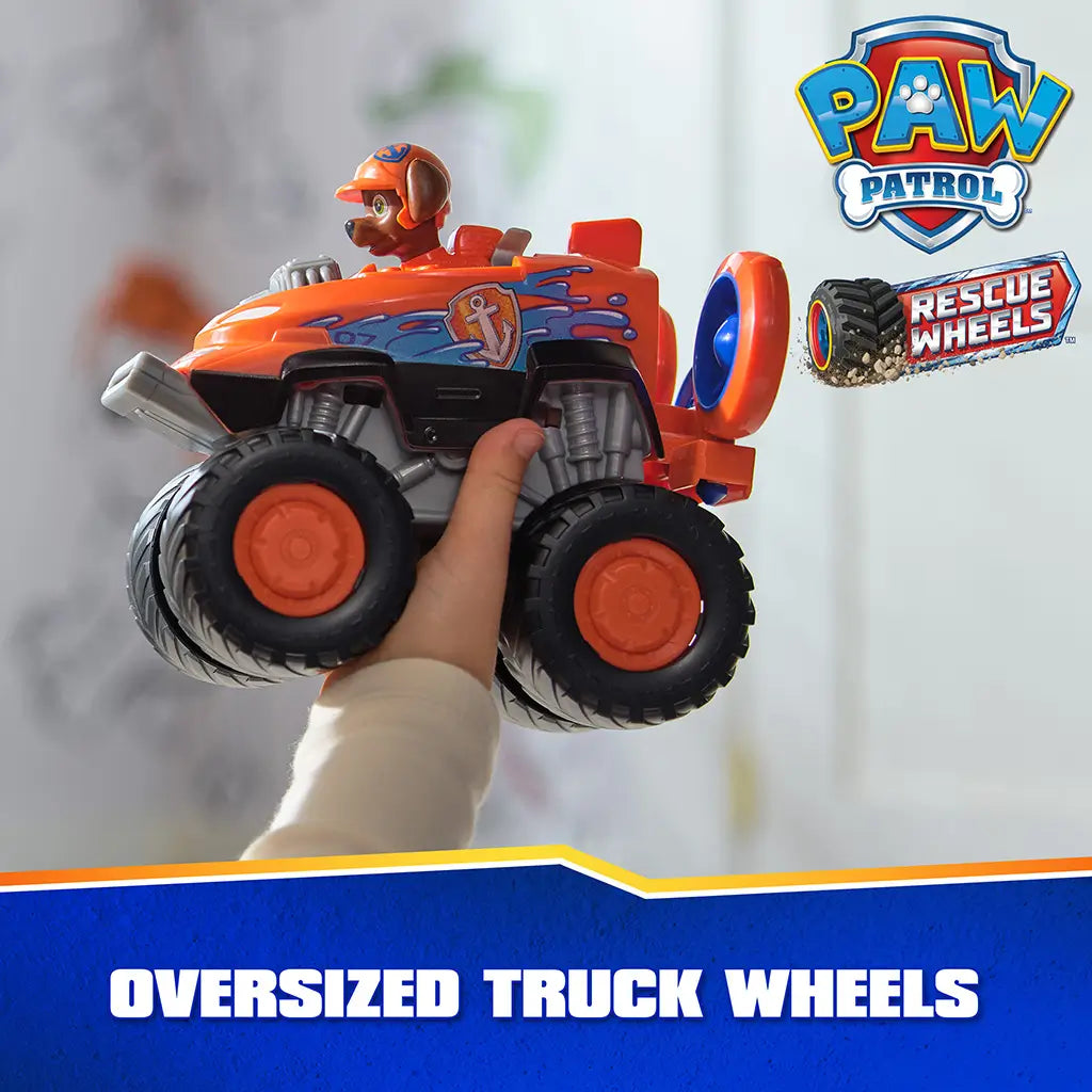 PAW Patrol Zuma hovercraft toy shows bright orange plastic body with smooth finish, large oversized truck wheels, and rear fan attachment, held in hand to highlight rugged design in indoor setting.